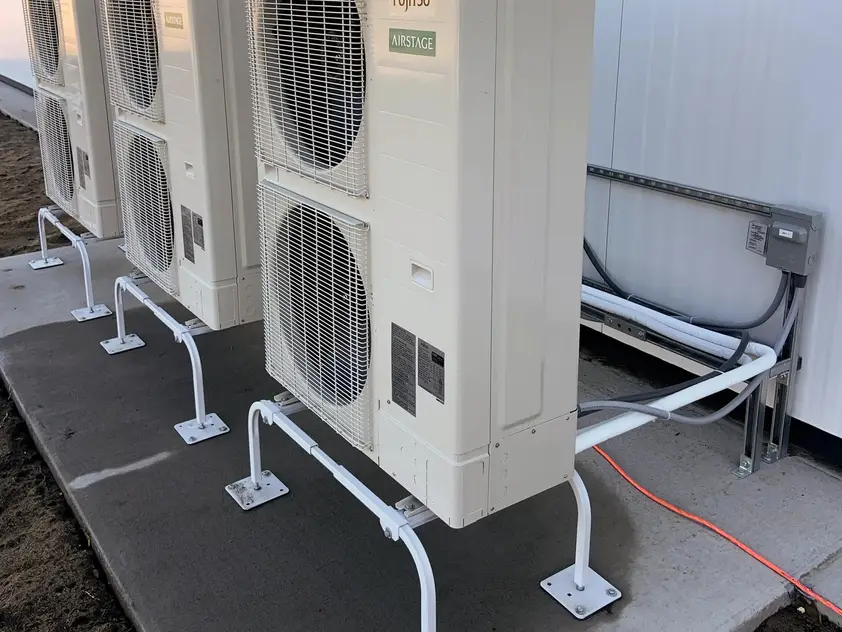 Unidades exteriores de bomba de calor sobre soportes metálicos junto a la pared de un edificio, con su conexión eléctrica