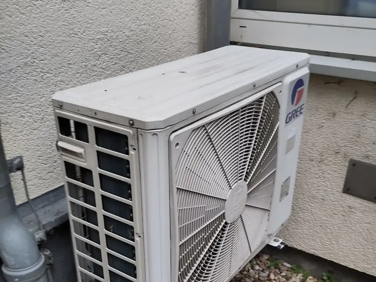 Unidad exterior de un split apoyada junto a la pared de una vivienda, con el ventilador a la vista